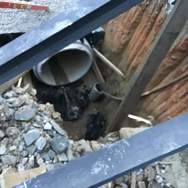 Construction site excavation showing large concrete drainage pipe and rubble with steel support beams.