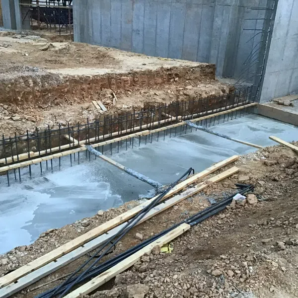 Concrete foundation slab with steel reinforcement bars and wooden supports at construction site excavated area.
