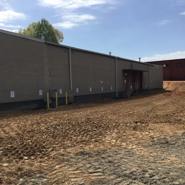 Back of large commercial building with dirt and tire tracks in foreground under clear sky.