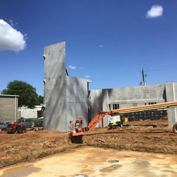 Construction site with concrete walls, orange lift equipment, excavated ground, clear sky with a few clouds.