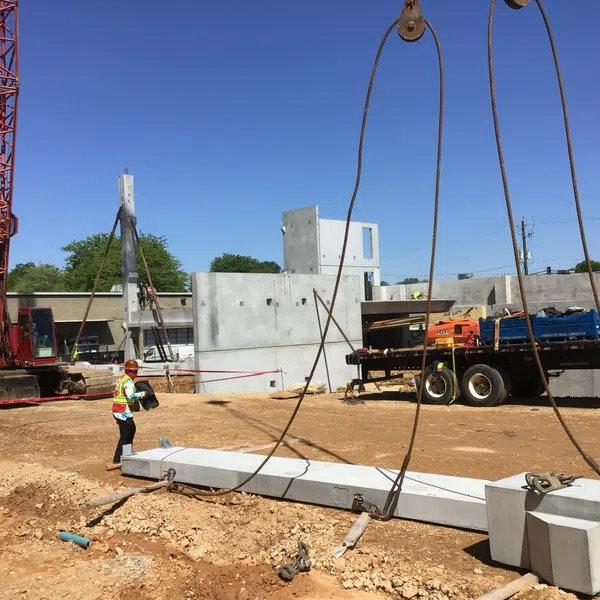 Construction site with workers guiding a large concrete beam being lifted by a crane under a clear blue sky