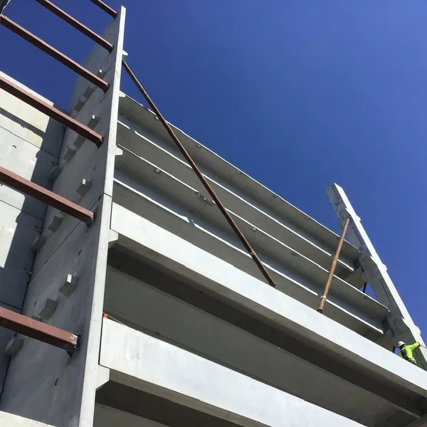 Low-angle view of an unfinished concrete building structure against a clear blue sky with metal supports.