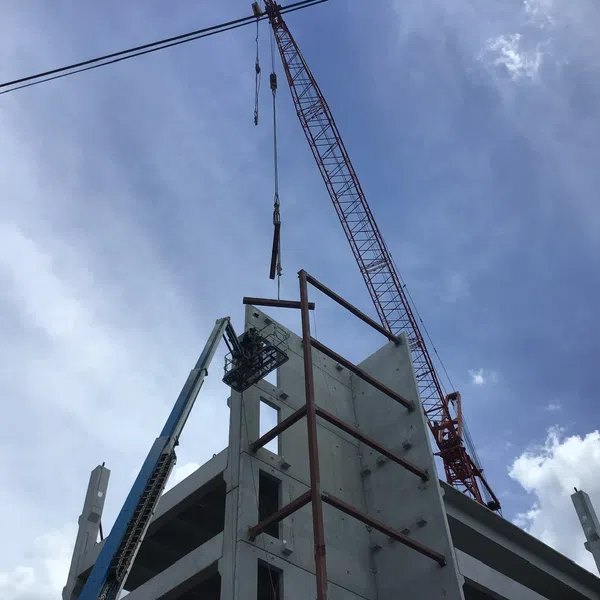 Construction site with crane lifting materials onto a steel-framed concrete building under blue sky with clouds