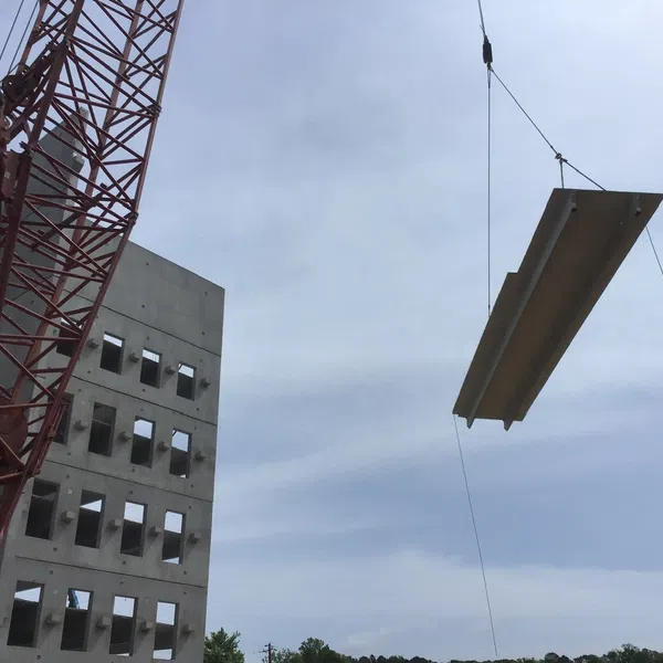 Crane lifting a large concrete slab near a multi-story building under construction on a cloudy day
