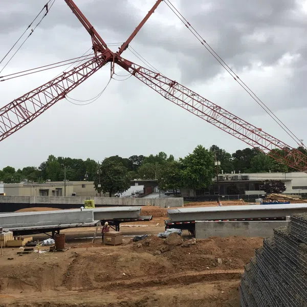 Construction site with large red cranes lifting concrete beams under a cloudy sky.