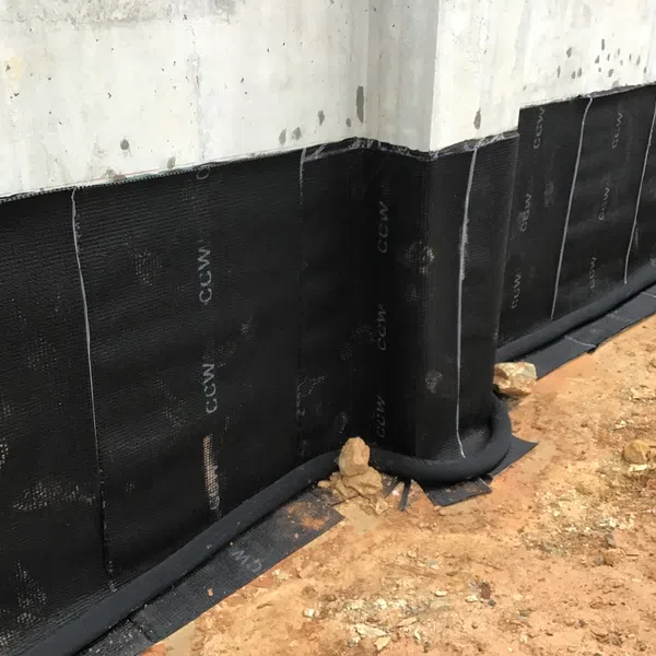 Black waterproof membrane applied to concrete foundation walls with dirt ground surrounding the area in construction site.