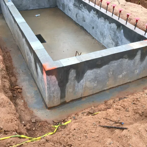 Concrete foundation walls set in an excavated construction site with soil and rebar exposed outdoors.