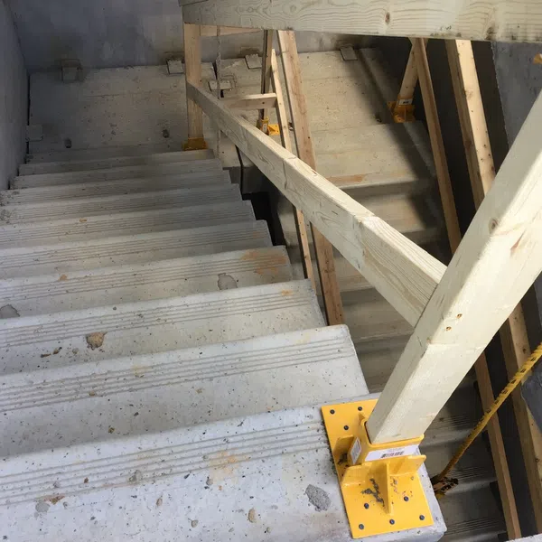 Concrete stairs under construction with wooden railings and yellow metal support brackets in a building site.