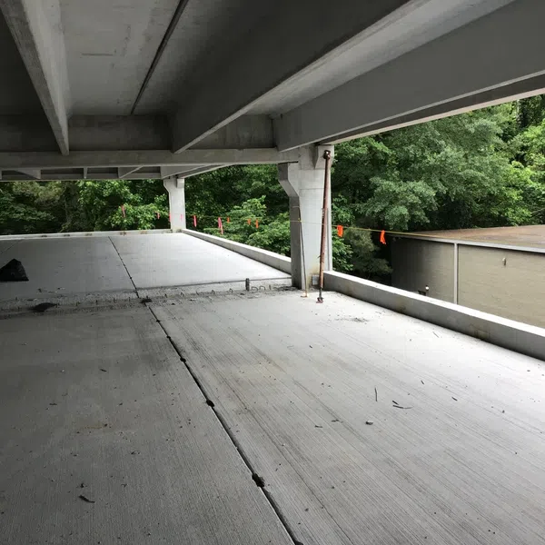 Empty concrete parking garage level with open sides showing adjacent building and green trees