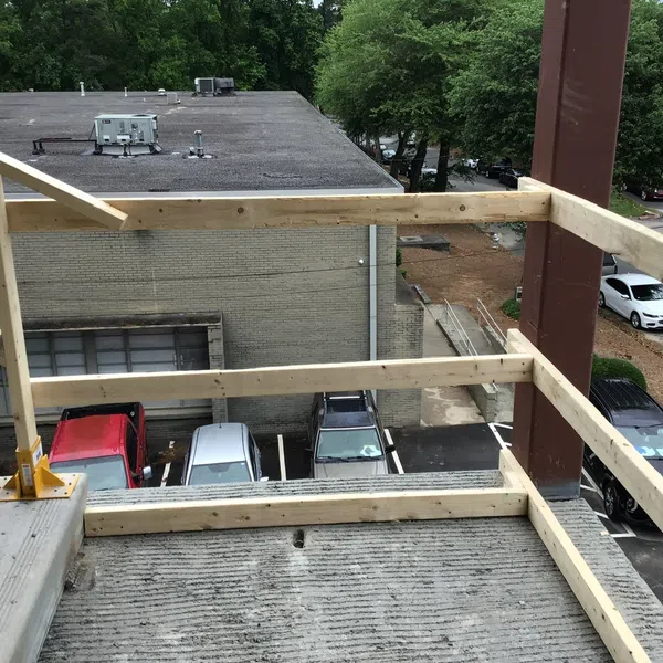 Wooden safety railing installed around concrete balcony overlooking a parking lot with cars and trees.