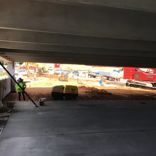 Construction site under a highway overpass with machinery and workers preparing the ground for development.
