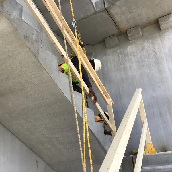 Construction worker in safety gear installing wooden handrails on concrete stairs at building site.
