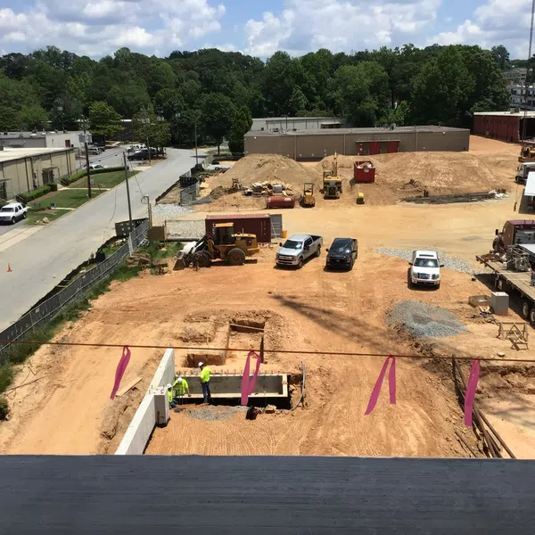Construction site with heavy equipment, vehicles, and workers preparing foundation under partly cloudy sky.