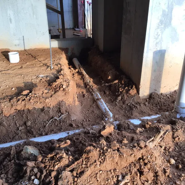 Construction site with exposed PVC drainage pipes and dug soil around concrete foundation pillars.
