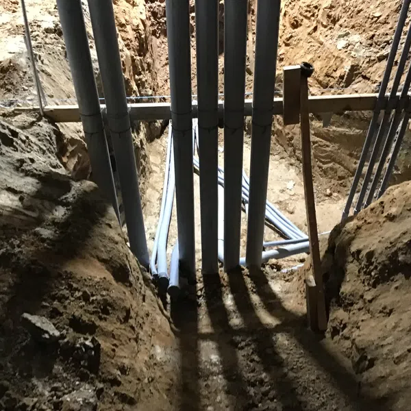 Trenched underground site with multiple PVC pipes installed for plumbing or electrical work under construction.