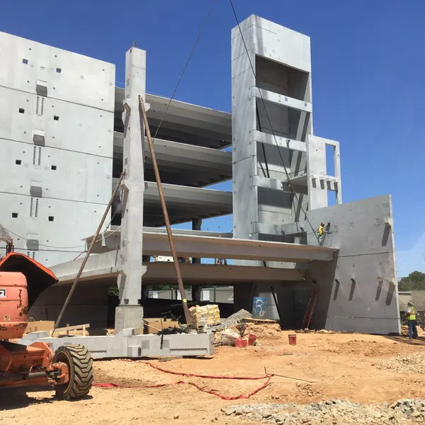 Construction site showing concrete framework of a multi-story building and heavy machinery under clear blue sky.