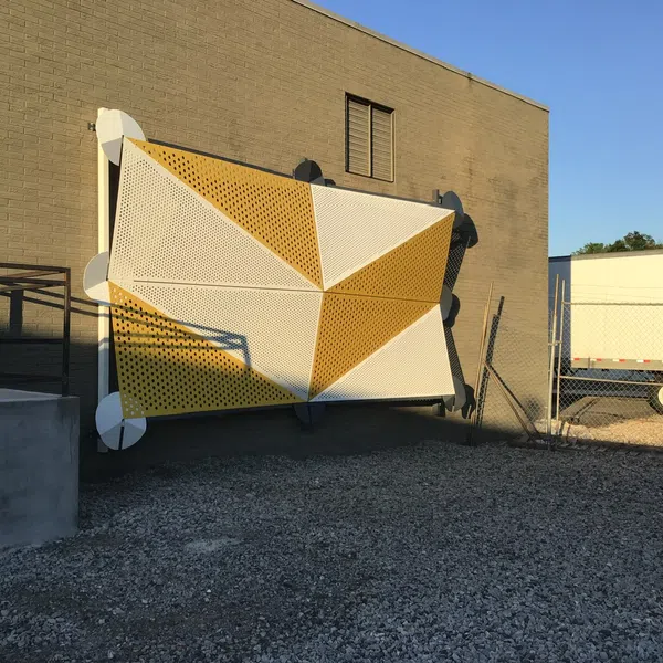 Large geometric yellow and white perforated metal panel mounted on an exterior brick wall next to a loading dock.