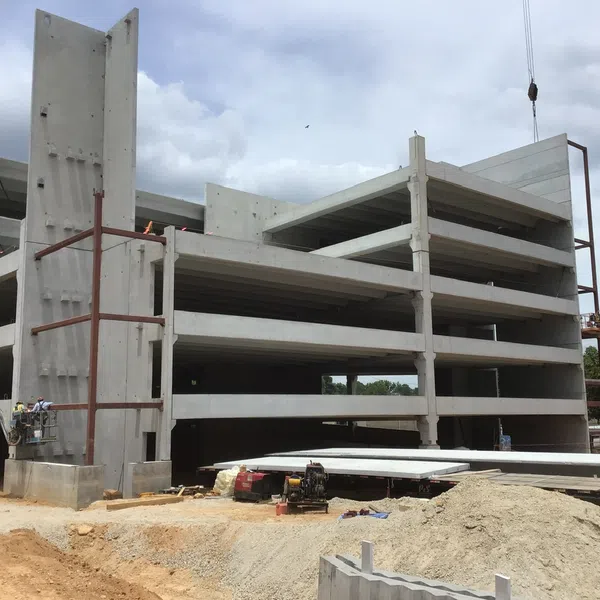 Multi-level concrete parking garage under construction with workers and machinery on a cloudy day