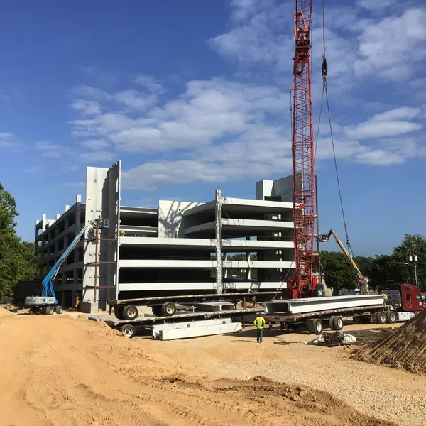 Construction site with a multi-level concrete parking garage under assembly and a large red crane lifting materials.