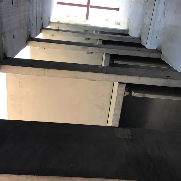 Looking upward through a concrete building structure with beams and a bright opening above