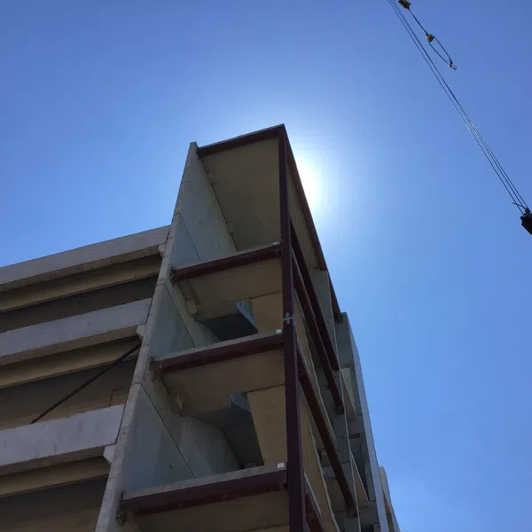 Under-construction concrete building structure with exposed floors against clear blue sky and sun behind corner.