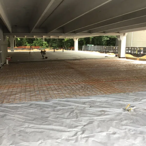 Construction site under a concrete parking garage with rebar grid and plastic sheeting on the floor