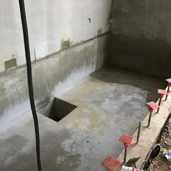 Concrete construction site with rebar and red safety caps along the edge next to a square hole in the floor.