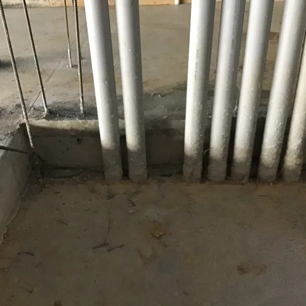 Concrete floor with several vertical metal pipes emerging from a recessed trench in an unfinished industrial space.