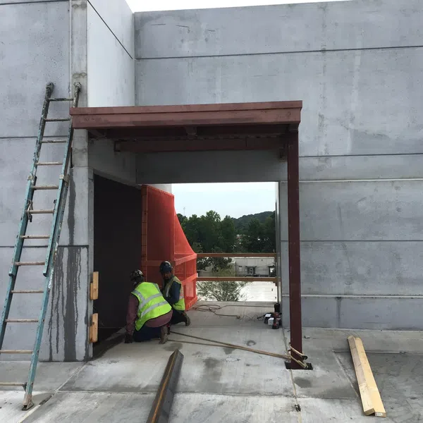 Two construction workers in safety vests working on a concrete building site with a metal ladder and wooden beam nearby