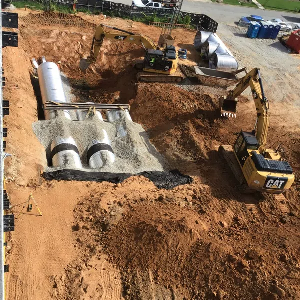 Construction site with excavators installing large corrugated drainage pipes and gravel base for stormwater management.