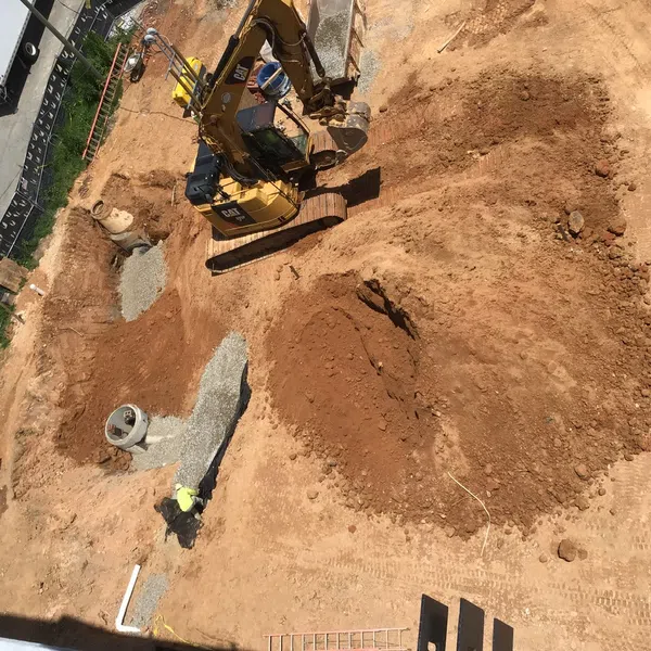 Construction site with excavator digging soil and worker preparing foundation trenches filled with gravel.