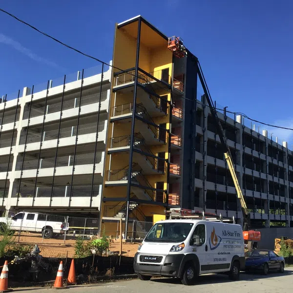 Multi-level parking garage under construction with workers and vehicles including a white service van and trucks.