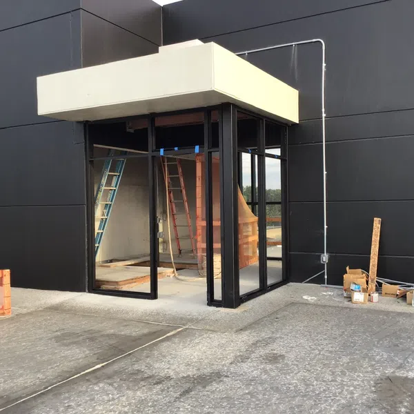 Black modern building exterior with glass entrance under beige canopy, construction materials, and ladders visible inside.