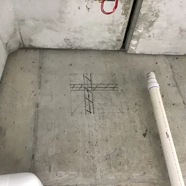 Concrete floor with plumbing pipe and marked construction layout lines for installation or cutting.