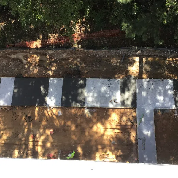 Overhead view of black and white tiled walkway under construction with dirt and surrounding greenery