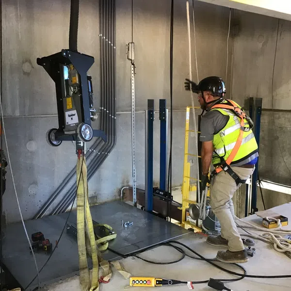 Construction workers in safety gear operate lifting equipment inside a concrete building under construction.