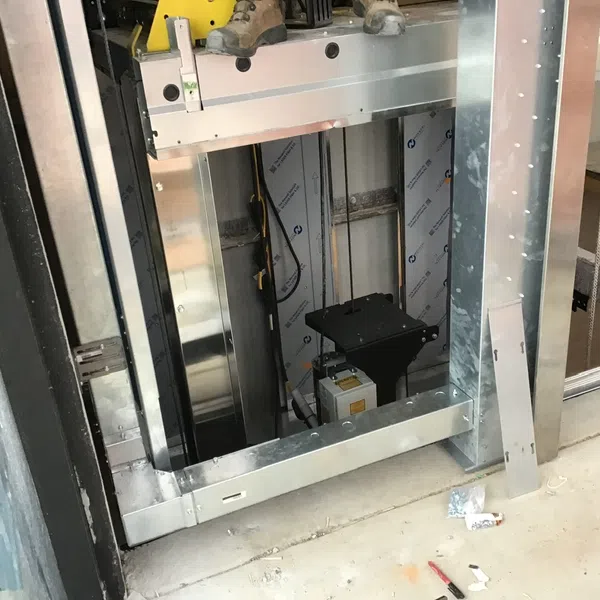 Construction site showing elevator shaft with metal framing and worker's boots visible above opening