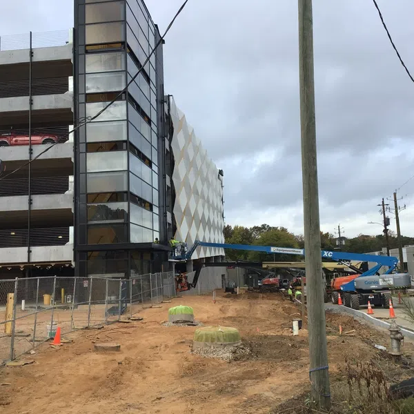 Construction site with workers installing facade panels on a multi-story parking garage under cloudy sky.