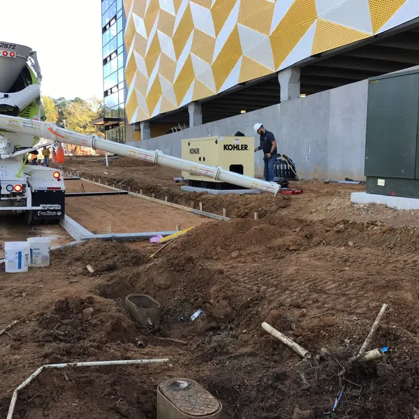 Concrete truck pouring cement at a construction site near modern building with yellow geometric facade and dirt ground