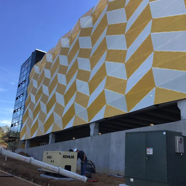 Building under construction with yellow and white geometric panel facade against blue sky.