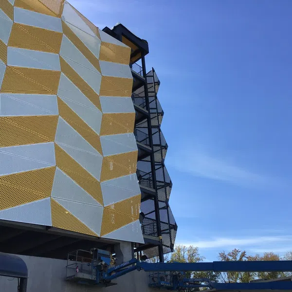 Modern building facade with geometric yellow and white panels and black metal staircases under clear blue sky