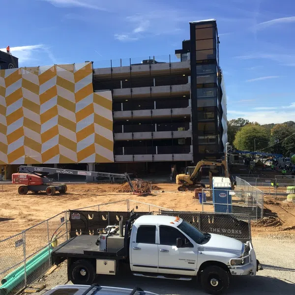 Construction site with a white flatbed truck, fenced area, machinery, and a building with a bold yellow and white geometric pattern.