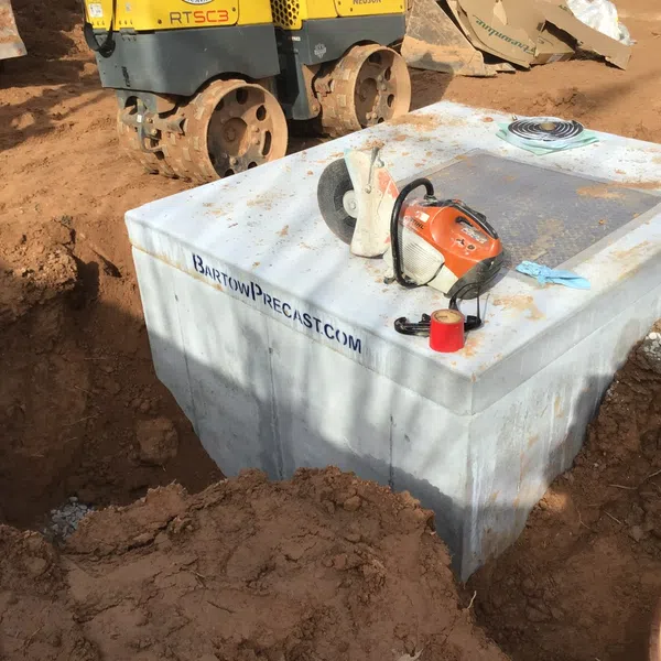 Concrete precast structure being installed on a construction site with cutting tools on top and compactors nearby.
