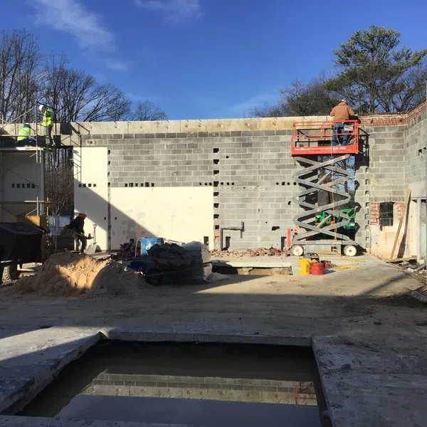 Construction workers building a concrete block wall on a sunny day with scaffolding and a scissor lift