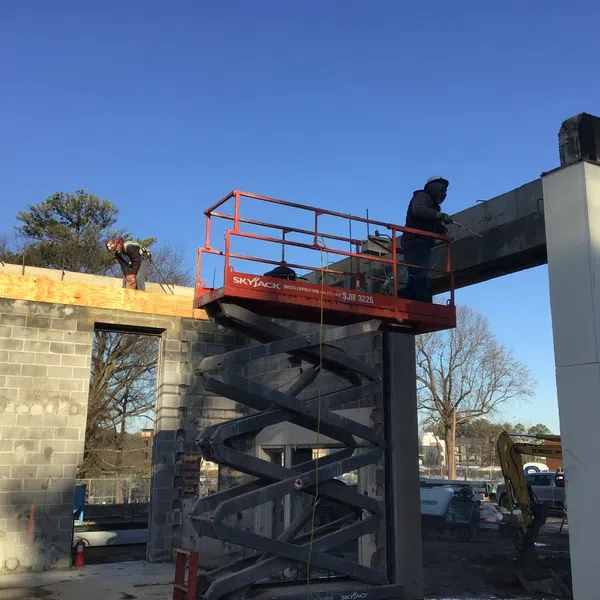 Construction workers using a scissor lift to work on a building structure under clear blue sky.