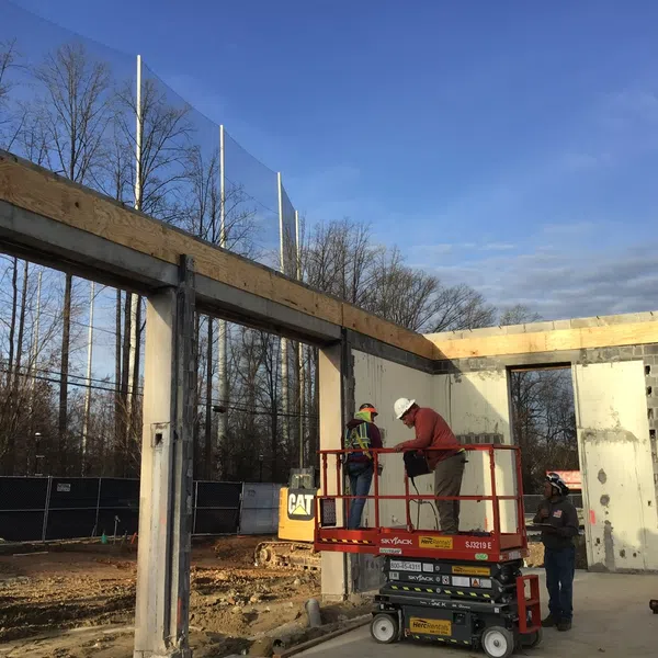 Construction workers on elevated platform assembling concrete building framework under clear sky.