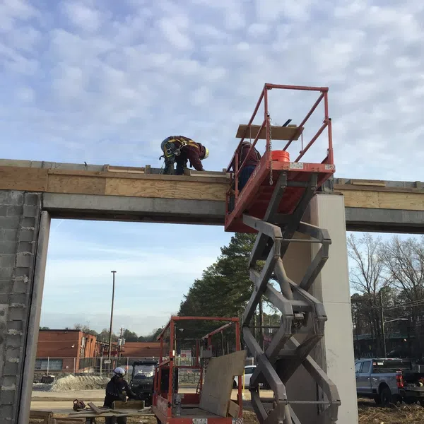 Construction workers on elevated platforms building concrete and wooden structure under a partly cloudy sky.