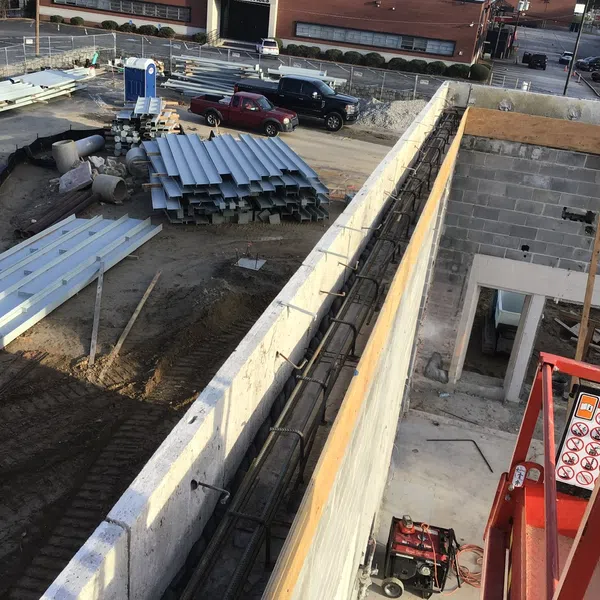 Construction site with concrete walls, steel beams stacked, and red machinery on a sunny day.