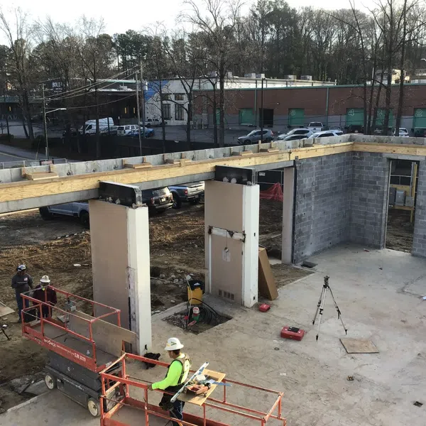 Construction site with workers, scaffolding, concrete pillars, and steel beams under clear daylight conditions.