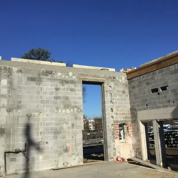 Partially constructed concrete block walls under clear blue sky with open door and window frames on building site.